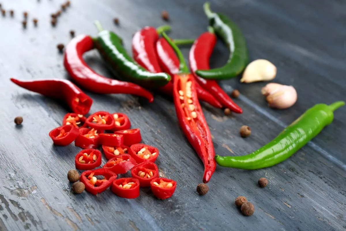 Sliced red chilies, whole green chilies, garlic, and peppercorns on wood.