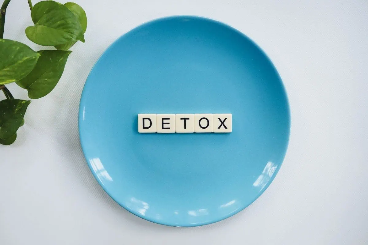 DETOX letter tiles on a blue plate with green leaves.