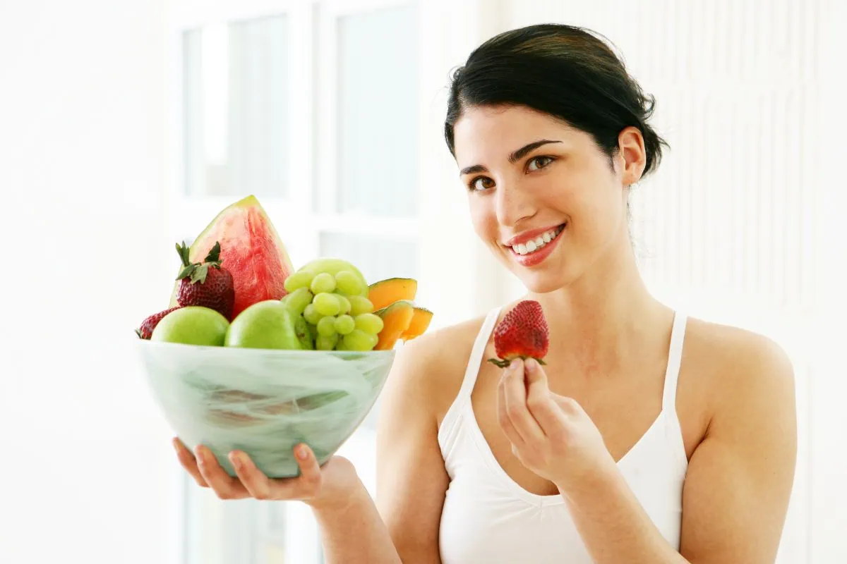 Smiling woman holding a fresh fruit bowl and a strawberry.