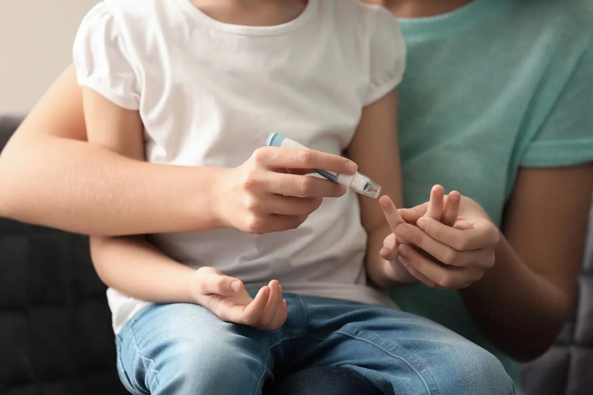 Adult checking child's blood sugar with a lancing device.