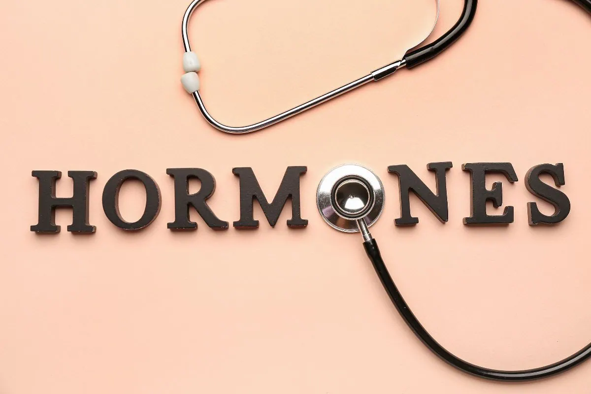 Stethoscope resting on the word HORMONES on a pink background.