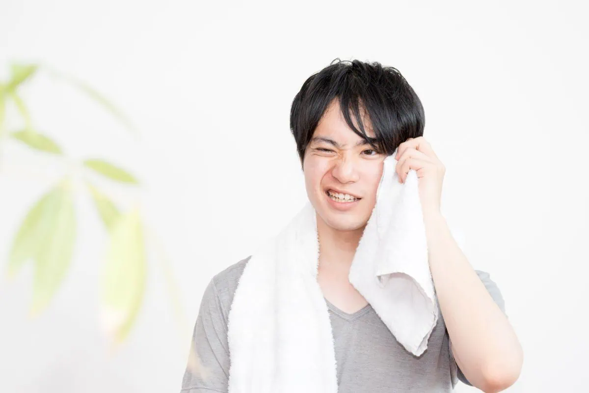 Young man wiping sweat from his face with a white towel.
