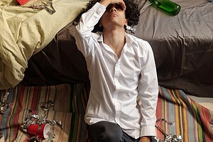 Exhausted person holding head sitting on floor amid party debris.