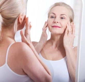 Mature woman touching her facial skin while looking in a mirror.