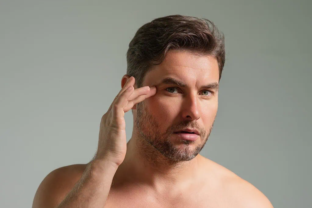 Man touching skin near eye examining facial wrinkles.