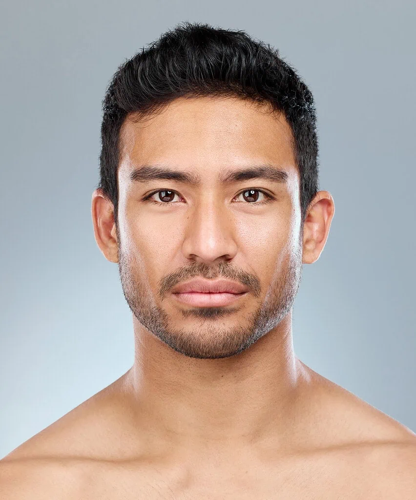 Close-up portrait of young man with clear skin and stubble.