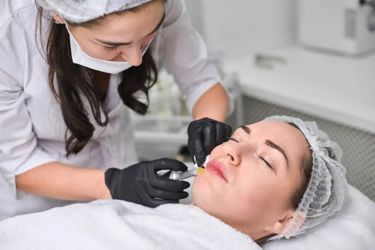 Clinic practitioner administering cosmetic facial injection to a woman.