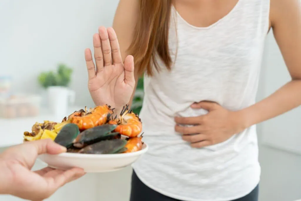 Woman rejecting seafood plate while holding her stomach.