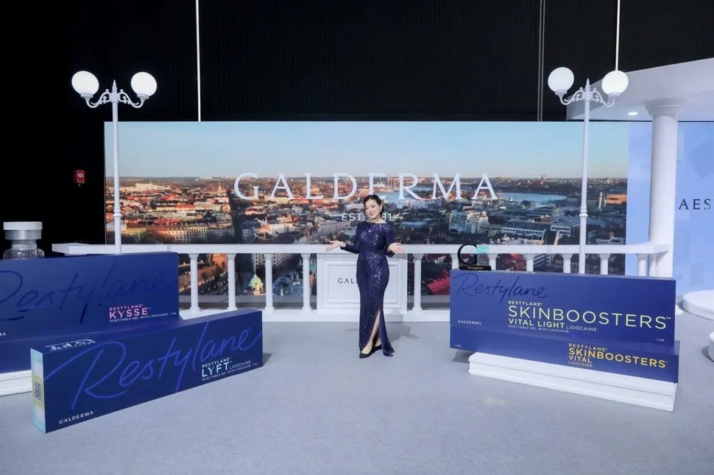 Woman presents cosmetic skin injectable products at an event with city backdrop.