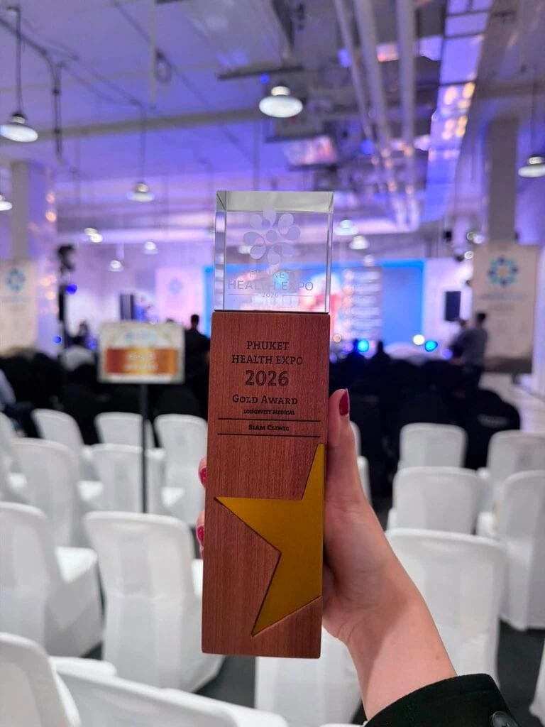 Person holding a glass award with a yellow star design at Phuket Health Expo 2026, with an event stage and chairs in the background.