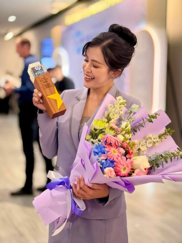 Woman in light purple suit holding a bouquet of flowers and a trophy at an award event.