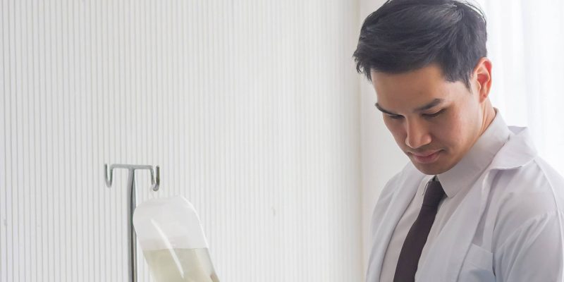 Male doctor in white lab coat checking an IV fluid bag on a stand.