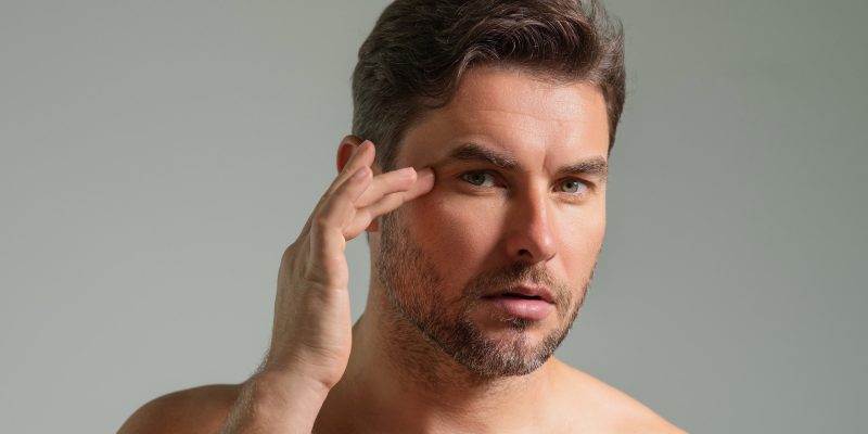 Man touching skin near eye examining facial wrinkles.