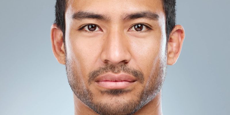 Close-up portrait of young man with clear skin and stubble.